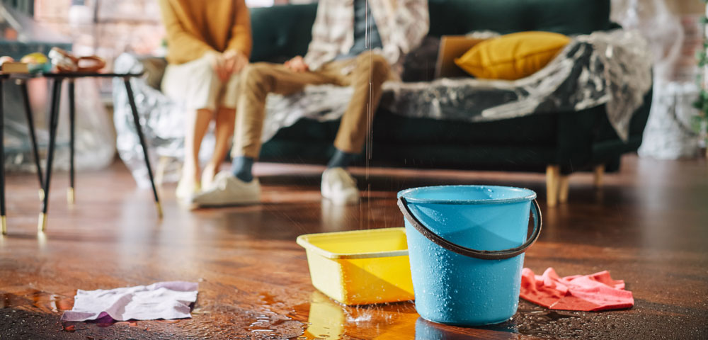 A photo showing water falling from the ceiling into buckets on a wood floor, with drips and rags all around