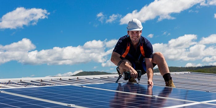 smiling man installing solar panels on a roof