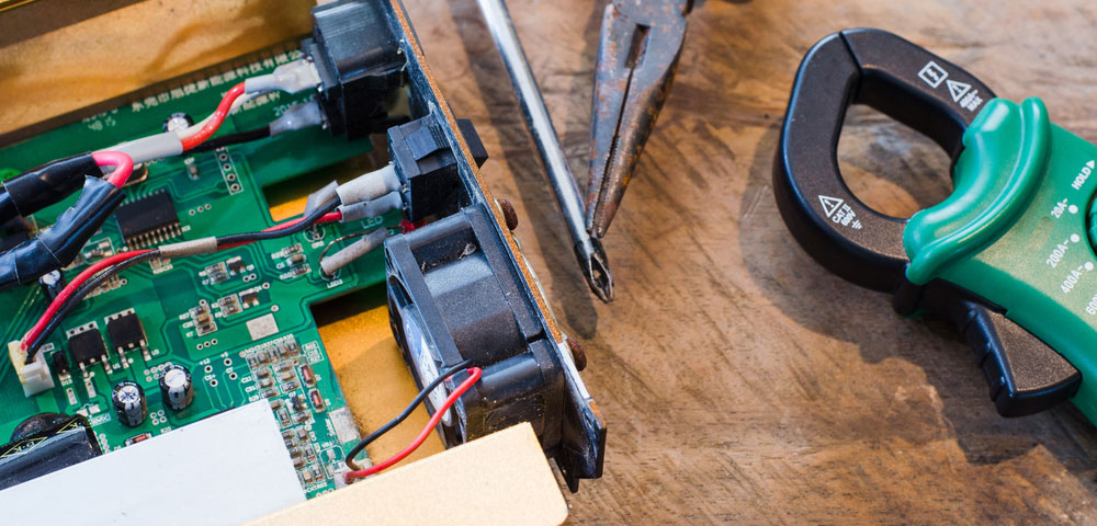 A photo showing a clamp-style multimeter and hand tools next to an open solar inverter