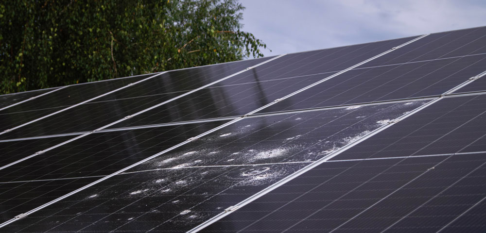 A photo showing an array of solar panels, with one panel damaged with large pockmarks from hail