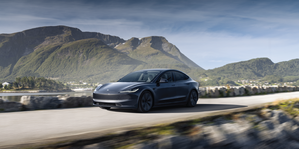 A grey Tesla Model 3 driving down a waterside highway